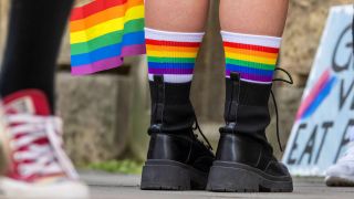 Ein paar Füße in schwarzen Stiefeln mit regenbogenfarbenen Socken (Quelle: IMAGO | Arnulf Hettrich)