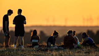 Junge Erwachsene sitzen auf dem Drachenberg in Berlin und schauen sich den Sonnenuntergang an (Quelle: IMAGO / Jochen Eckel)