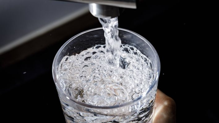 Wasser fließt aus einem Wasserhahn in ein Glas